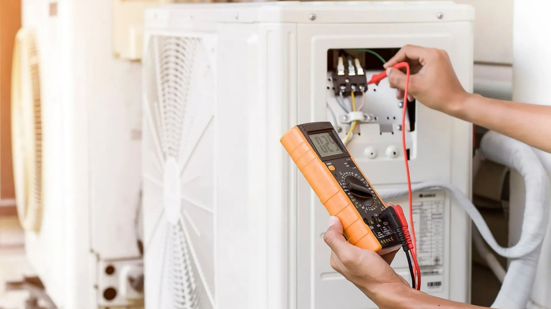 Personne utilisant un multimètre pour tester les connexions électriques d'un climatiseur.