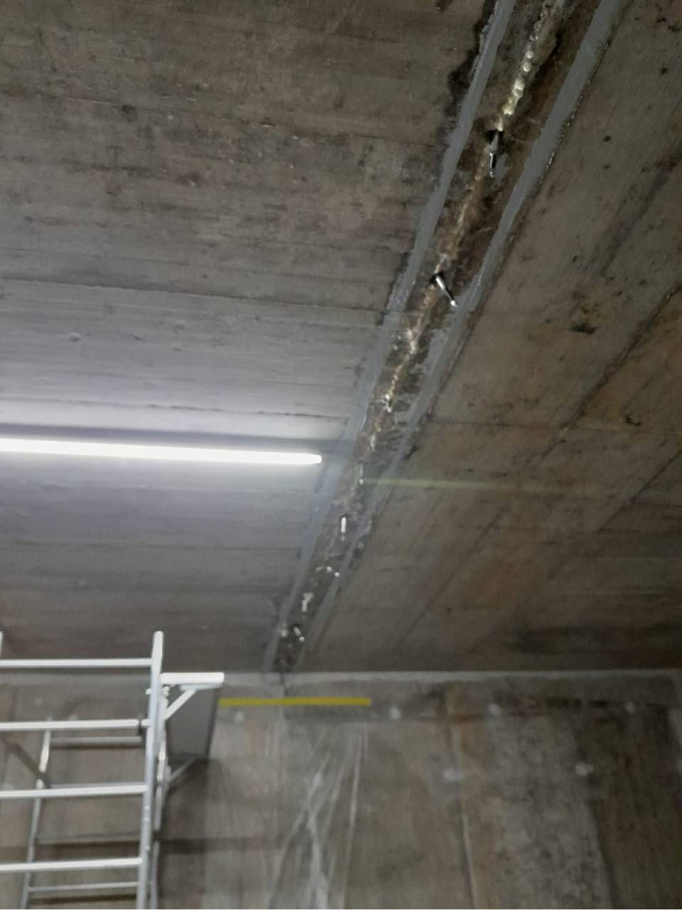 Plafond en béton présentant une longue fissure remplie d'un matériau brillant, avec un échafaudage visible.