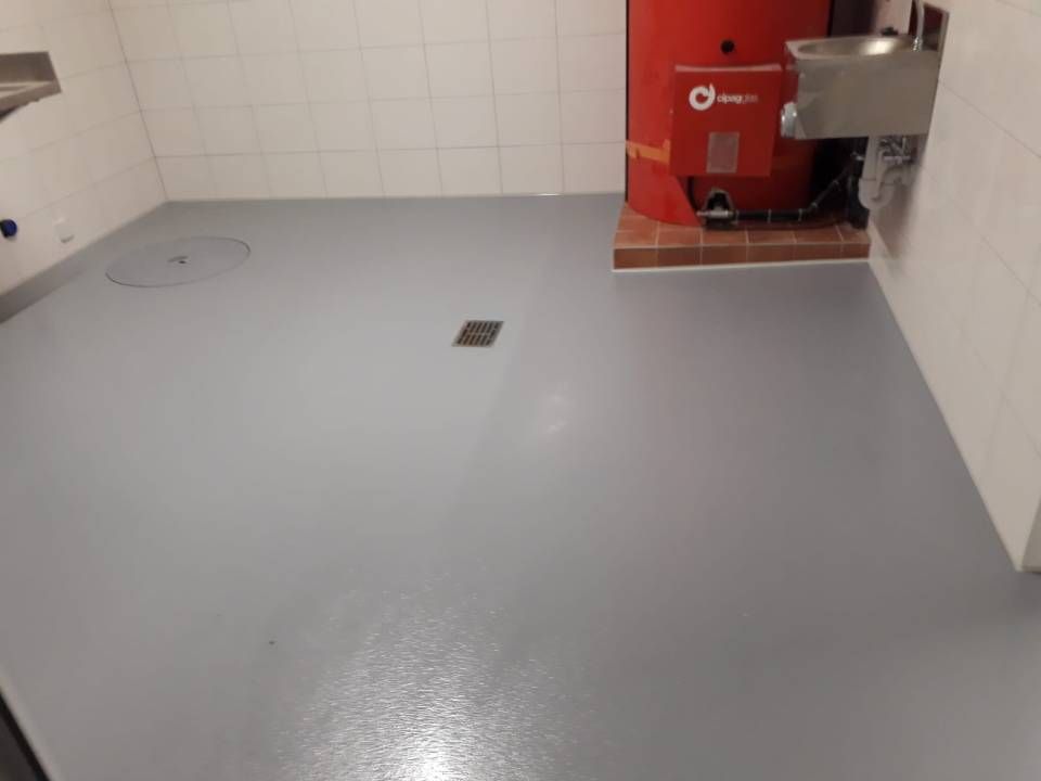 Sol peint en gris dans une buanderie avec une chaudière rouge, un évier en métal et des murs carrelés de blanc.