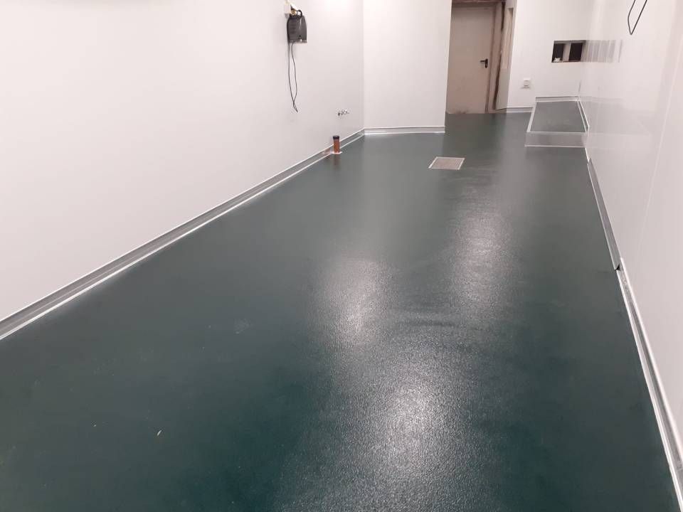 Sol vert foncé et brillant dans une pièce presque vide aux murs blancs et à l'encadrement d'une porte.