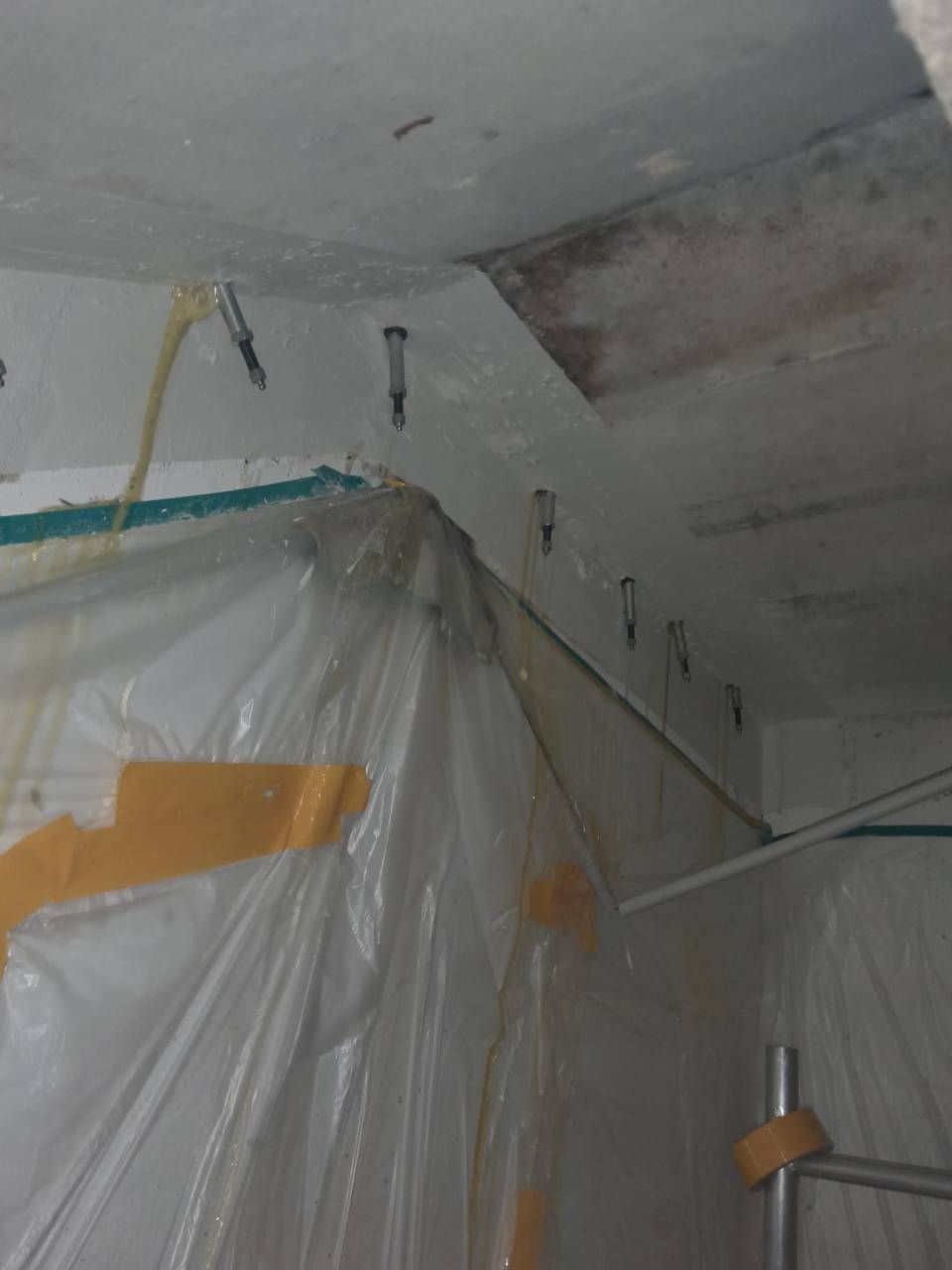 Une bâche en plastique et du ruban adhésif recouvrent un coin de la pièce, laissant apparaître le plafond.