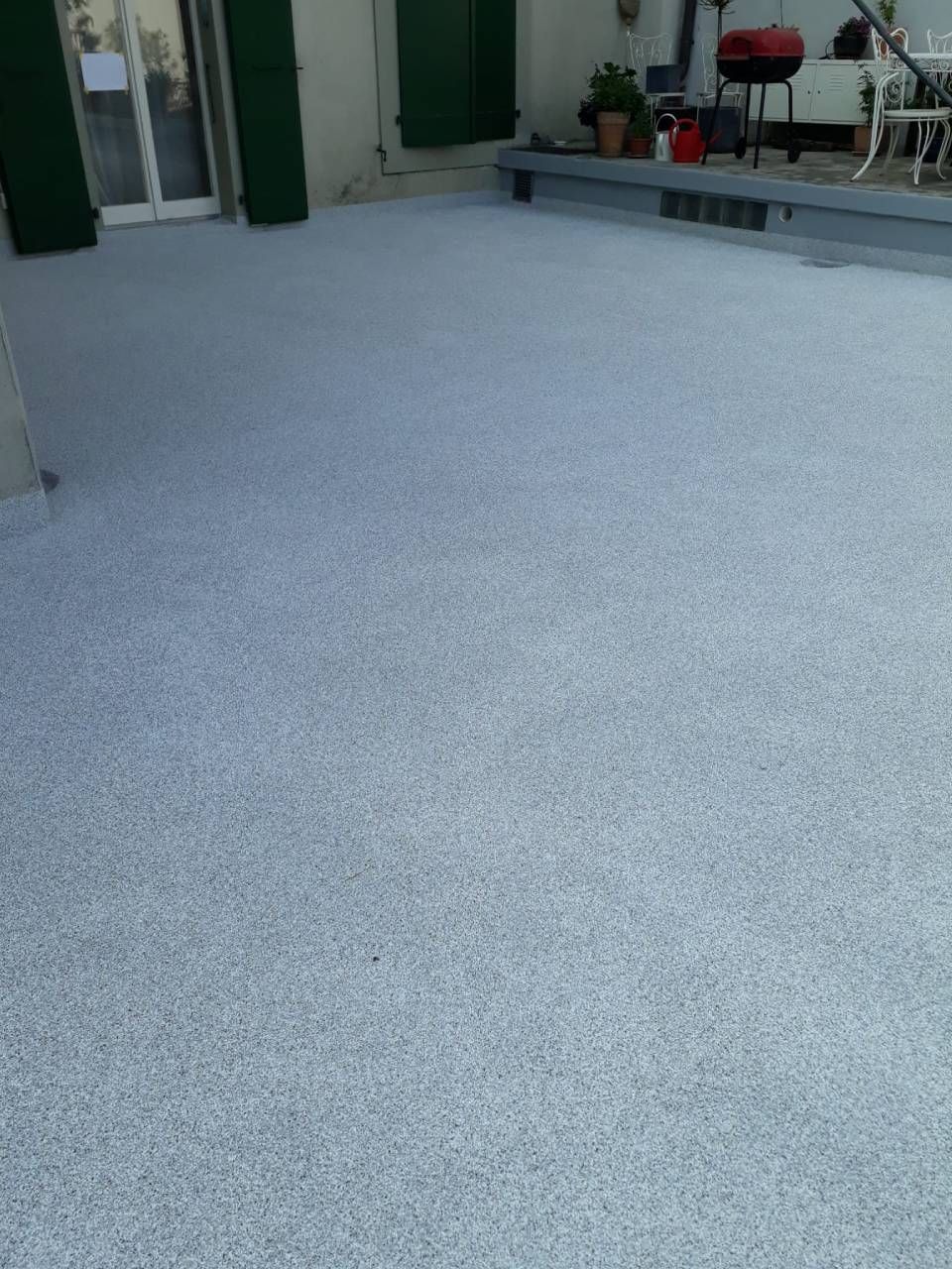 Un patio gris texturé avec des portes et des volets verts en arrière-plan.