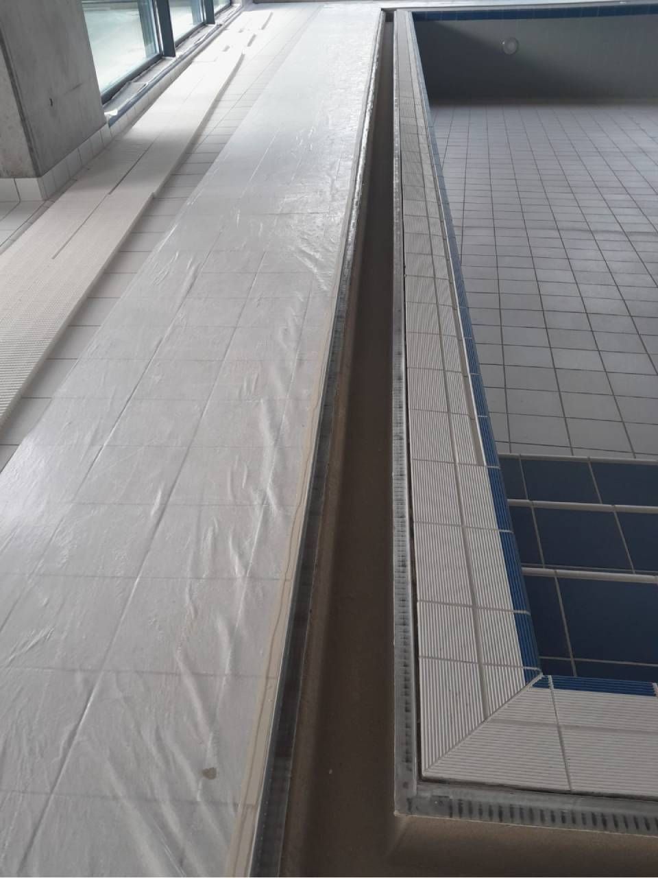 Piscine intérieure avec bordure carrelée et allée couverte.