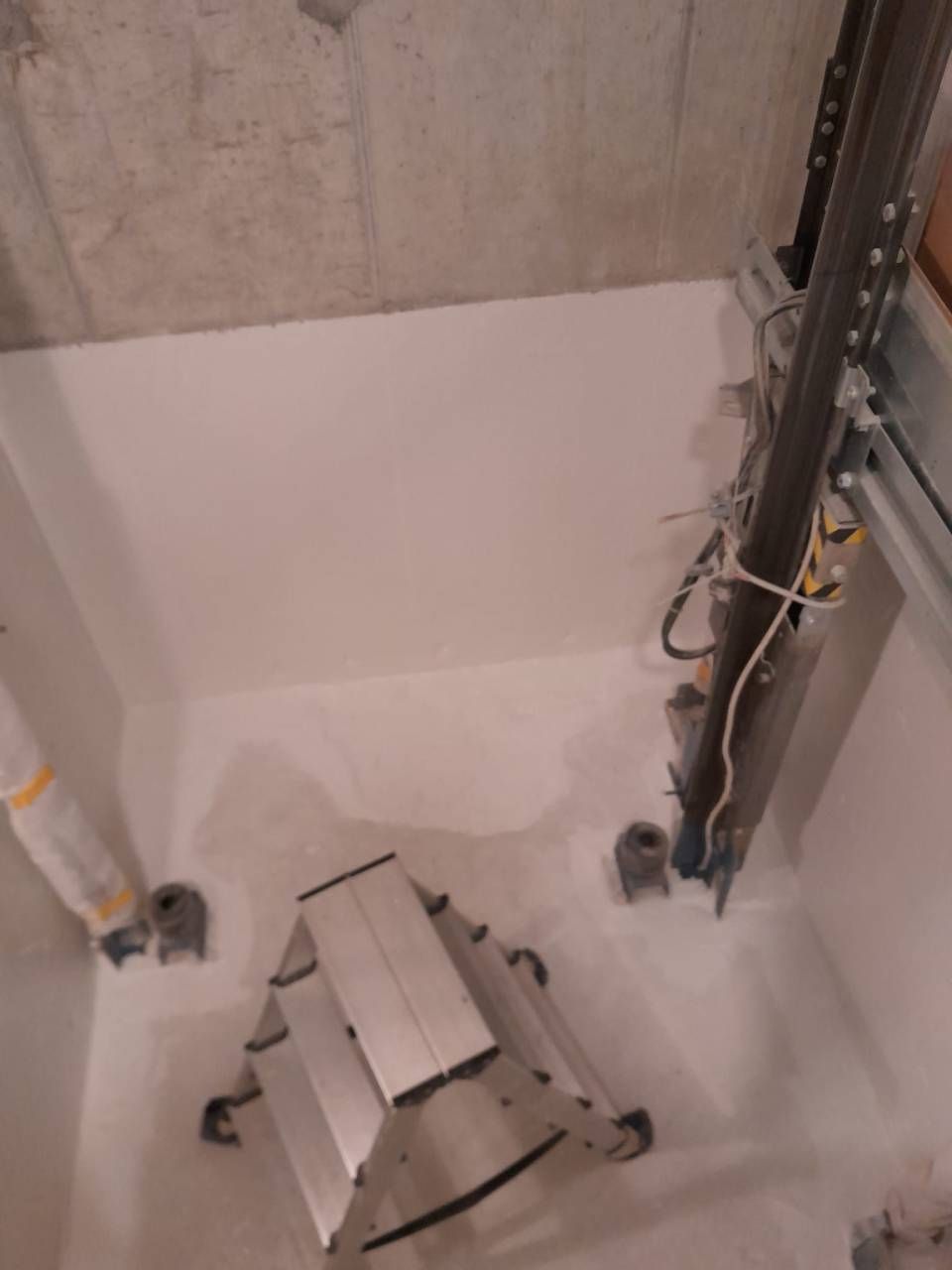Vue intérieure montrant une petite échelle à l'intérieur d'un caisson aux parois blanches, probablement un local technique ou utilitaire.