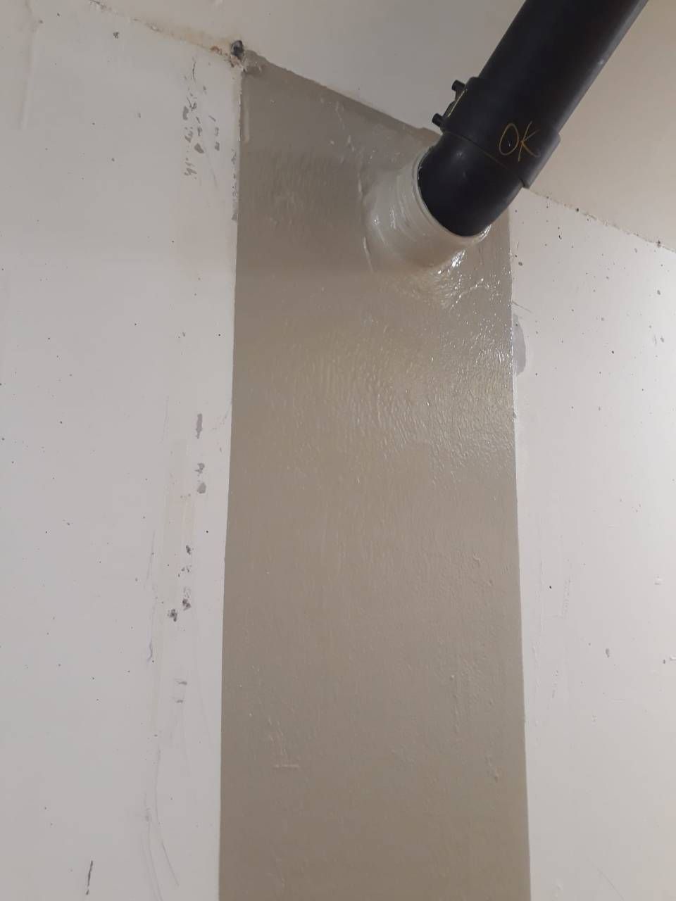 Un tuyau noir est inséré dans un mur peint en gris clair. Des murs blancs entourent l'angle.