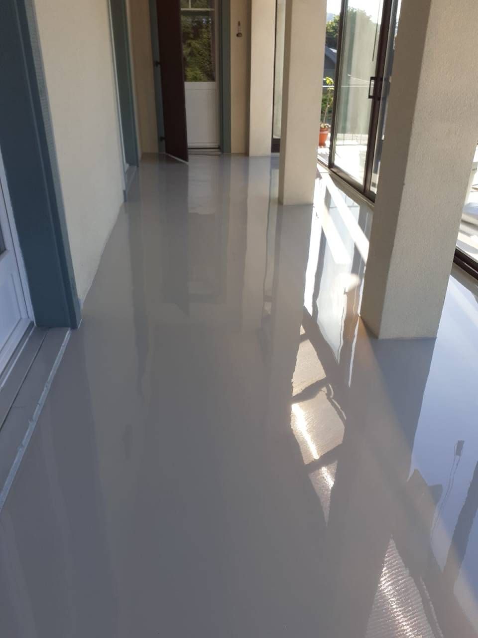 Un sol en époxy gris brillant reflète la lumière dans un couloir aux murs et colonnes blancs, et une porte.