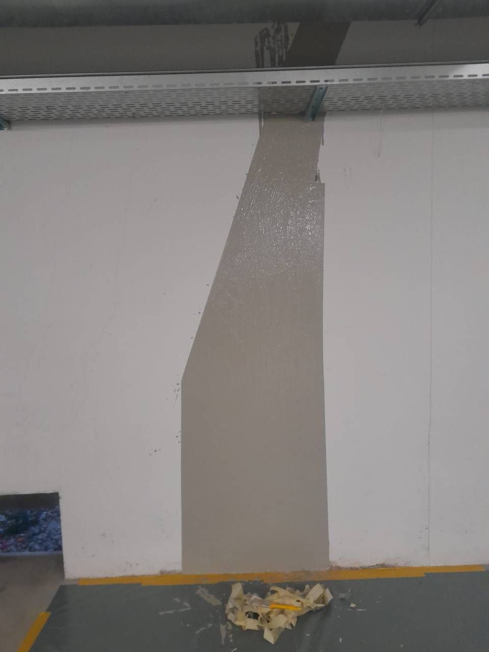 Une bande de peinture grise sur un mur blanc, avec un conduit électrique au-dessus et des débris en dessous.