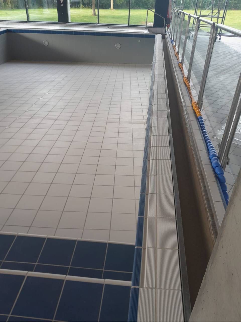 Piscine carrelée vide, avec des carreaux bleus et blancs.
