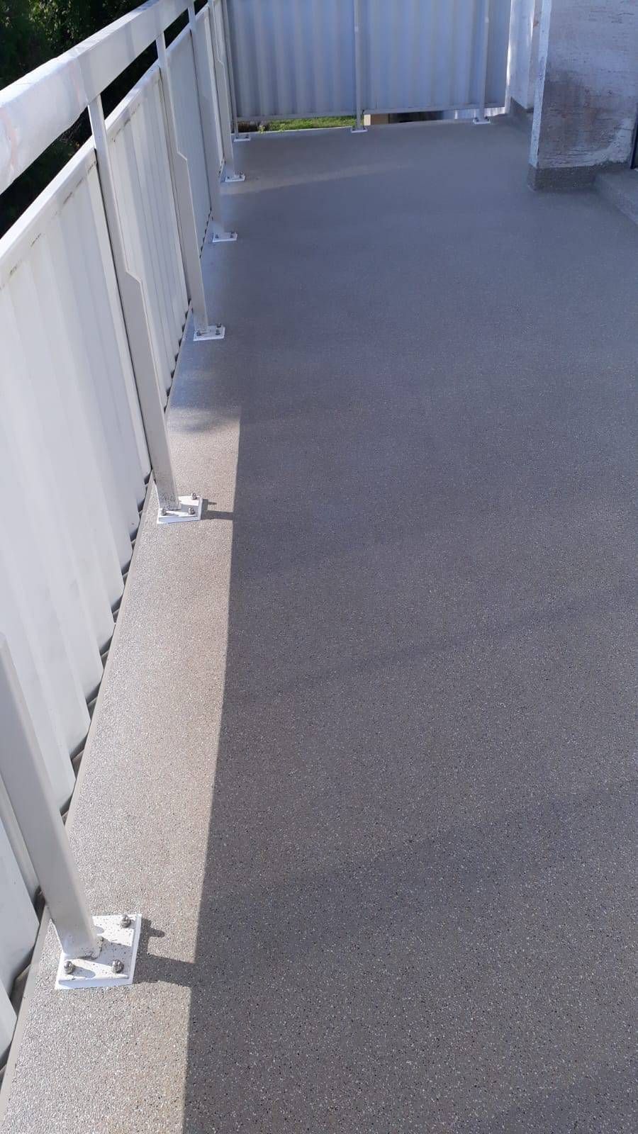 Allée extérieure grise avec rambardes blanches. Journée ensoleillée.