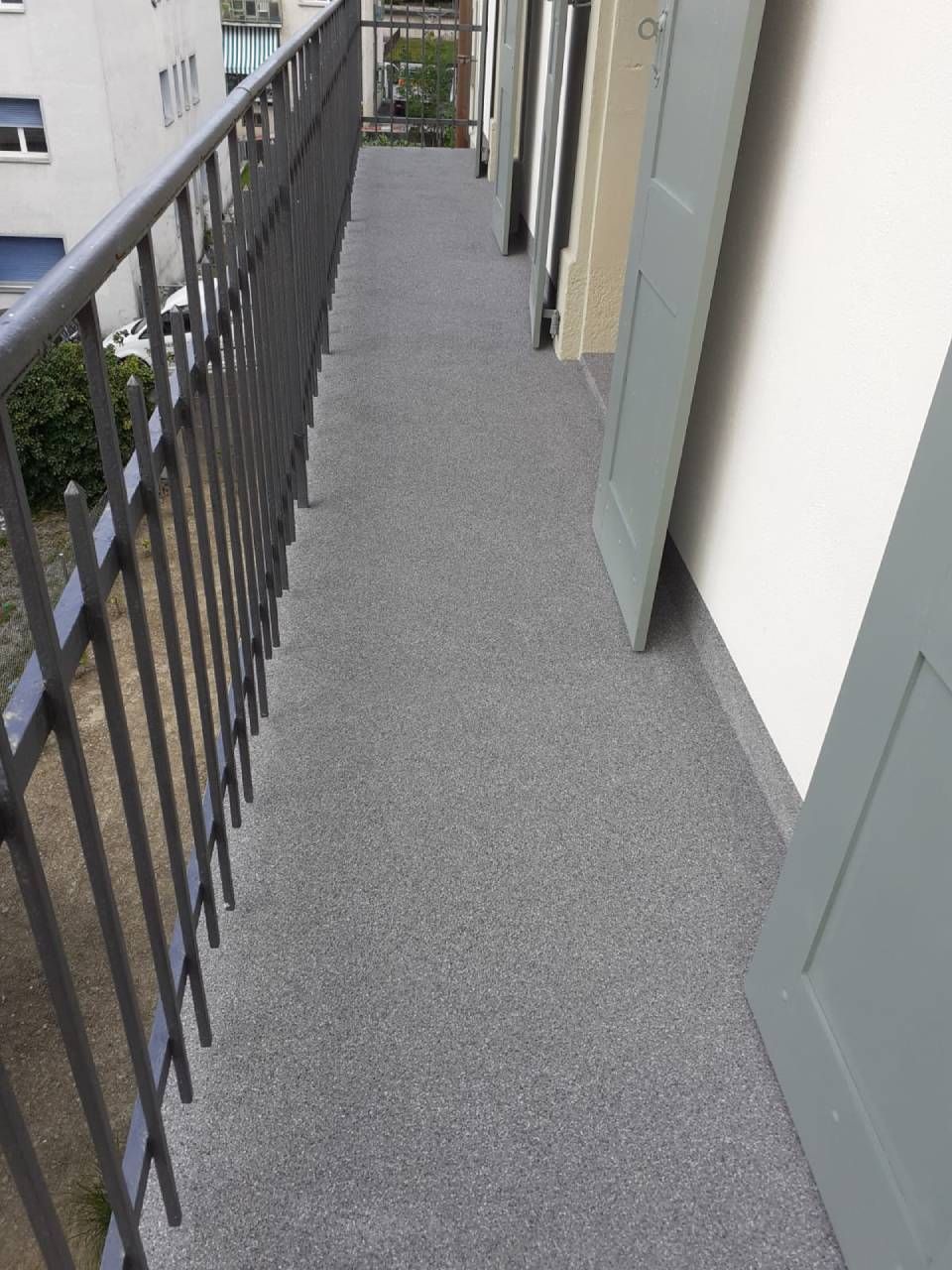 Un sol en époxy gris brillant reflète la lumière dans un couloir aux murs et colonnes blancs, et une porte.