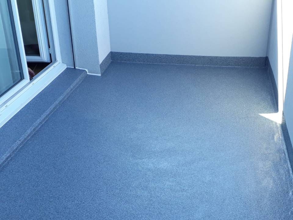 Le sol du balcon est moucheté de gris, assorti aux plinthes et aux murs blancs. Une porte-fenêtre coulissante se trouve à gauche.