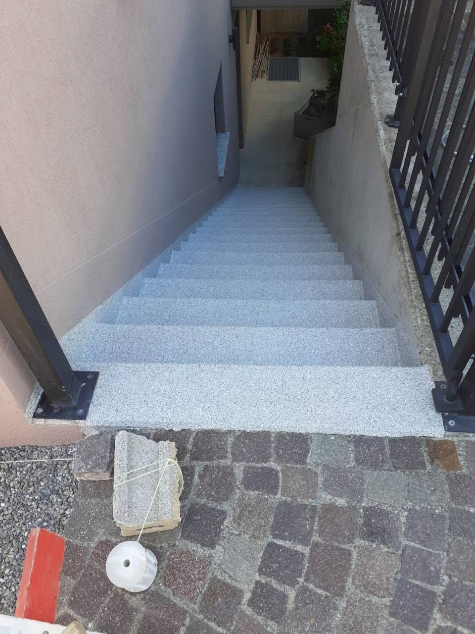 Escalier descendant, marches en béton entre un mur rose et une rambarde, le bas mène à un chemin pavé.