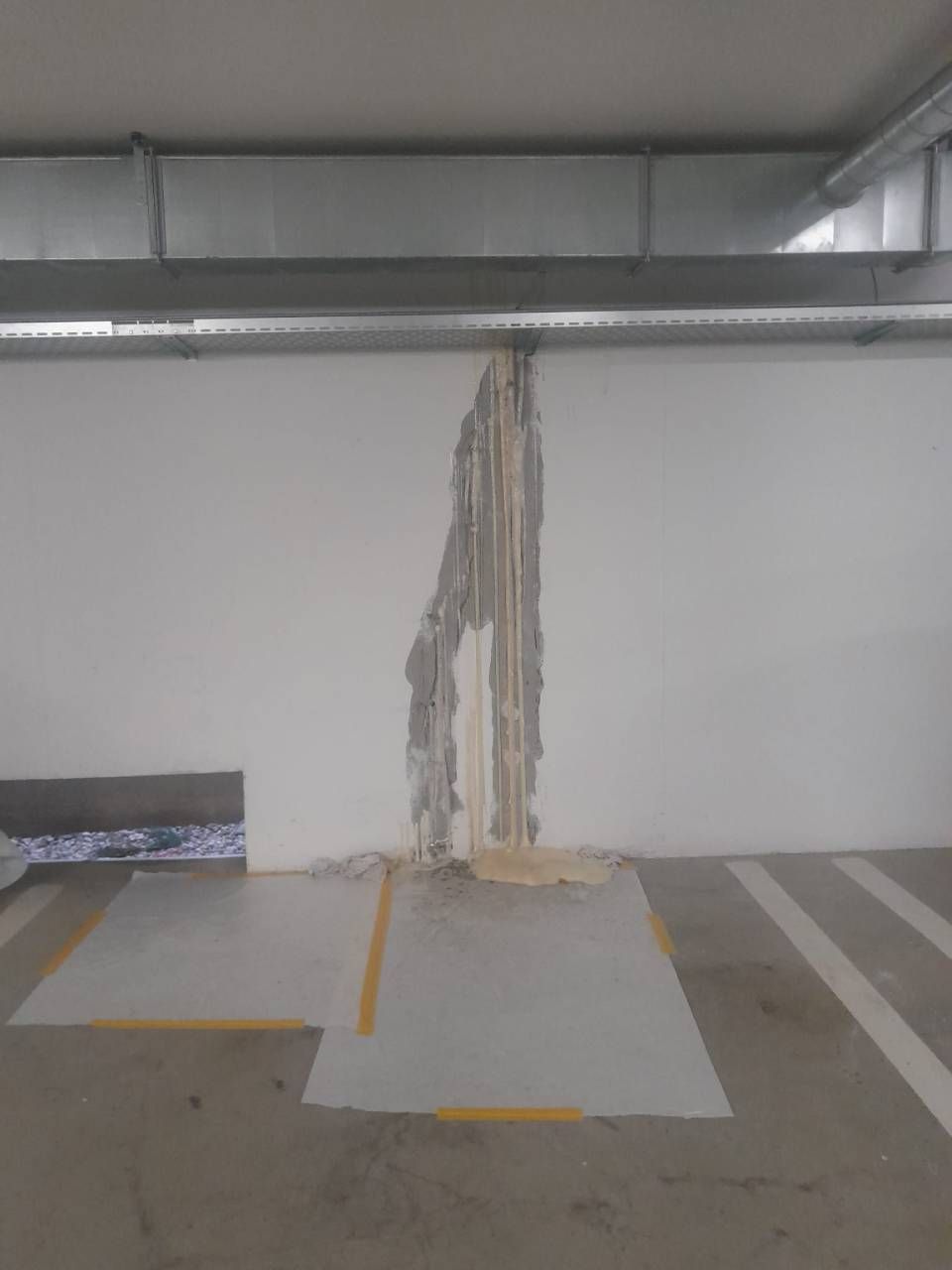 Mur intérieur endommagé dans un parking souterrain, avec câblage apparent, béton et structure métallique.