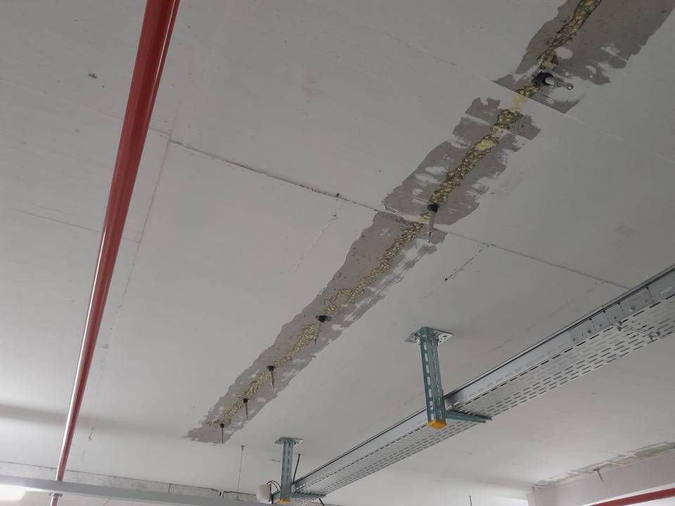 Plafond blanc avec câblage apparent et supports métalliques, tuyau rouge visible.