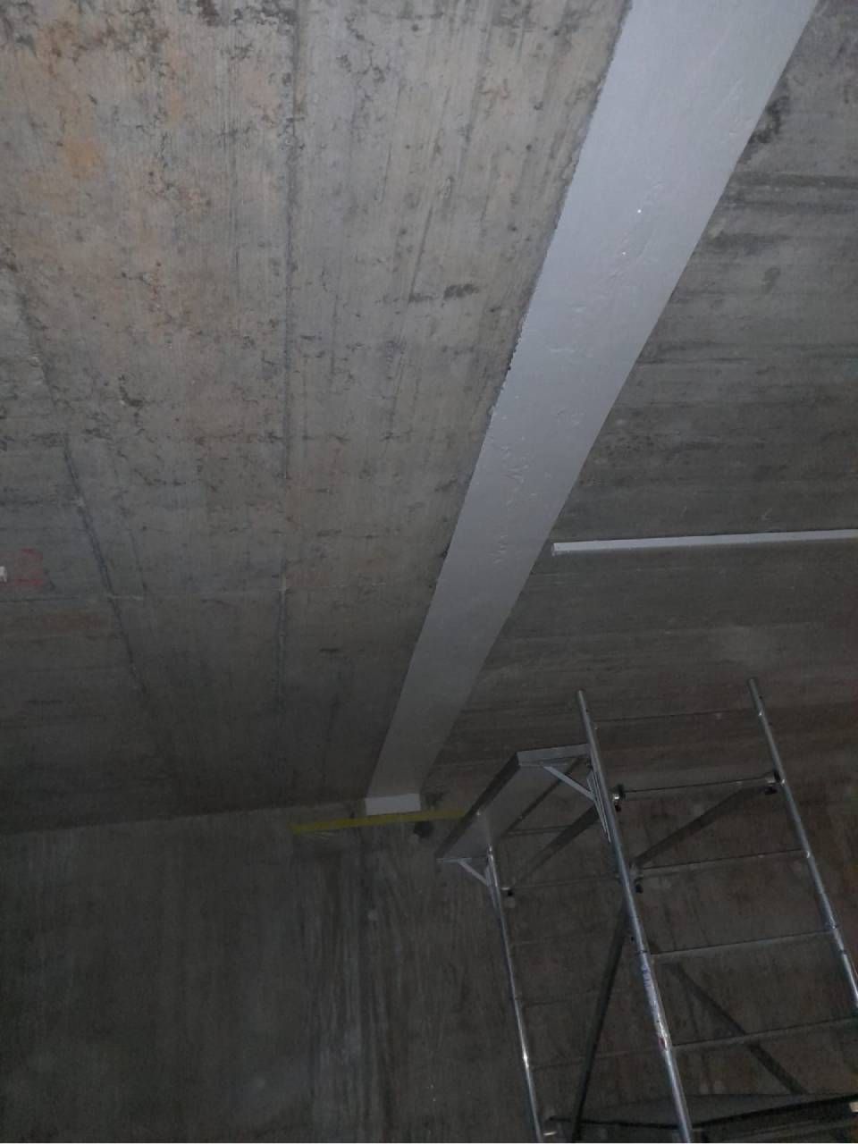 Plafond en béton avec une bande blanche au milieu. Des échafaudages sont visibles en bas à droite.
