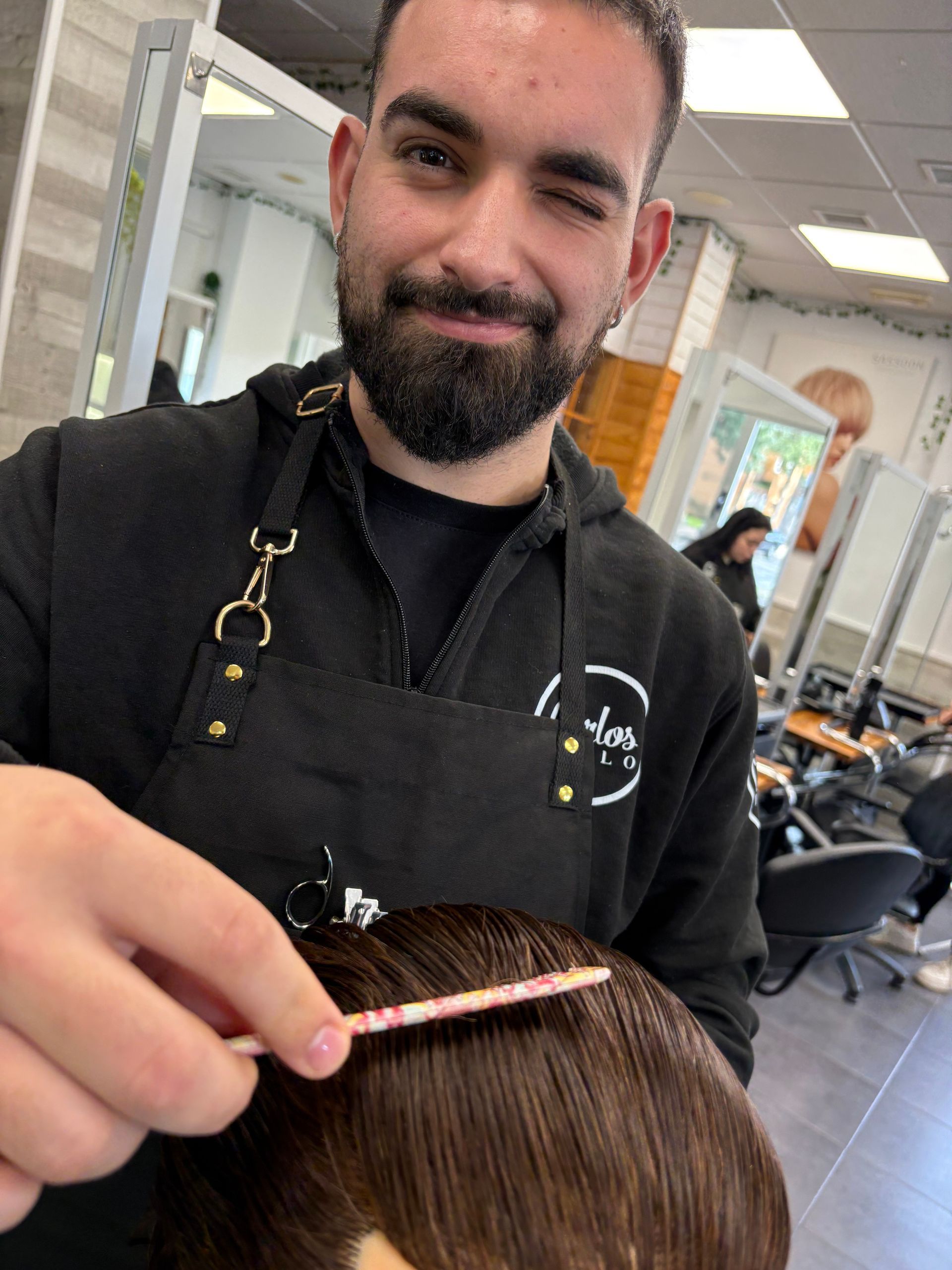 Una peluquera peina el cabello castaño de una clienta en una peluquería, con expresión concentrada.