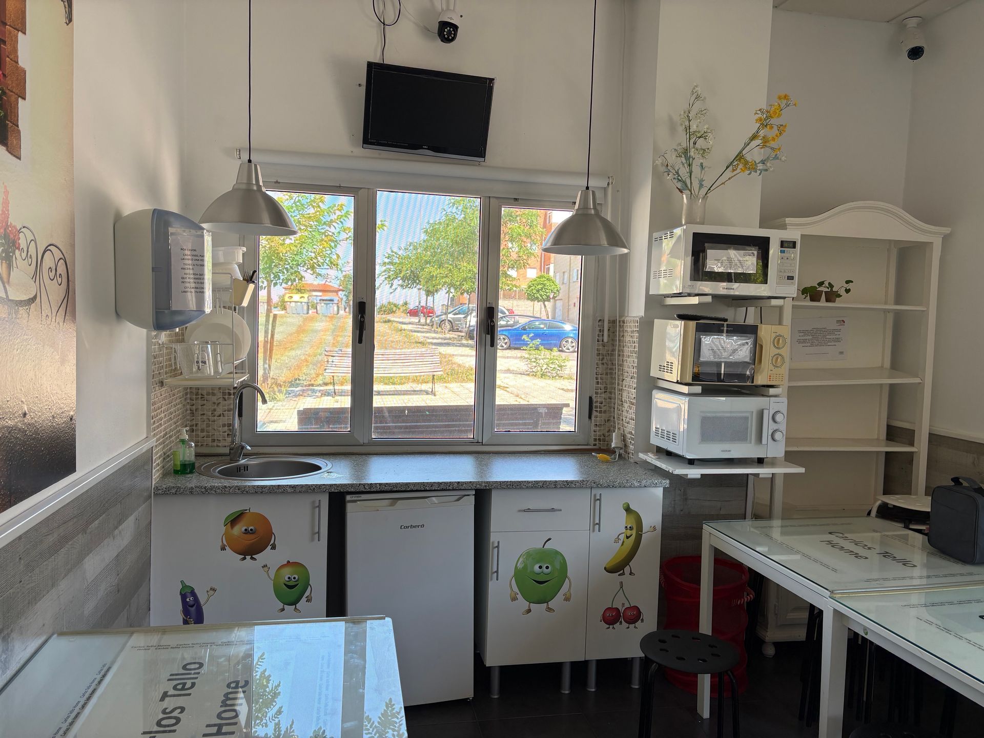 Cocina luminosa con ventana, armarios blancos, microondas, estantes y fregadero bajo la encimera.
