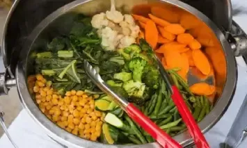 a pot filled with vegetables and tongs on a table .