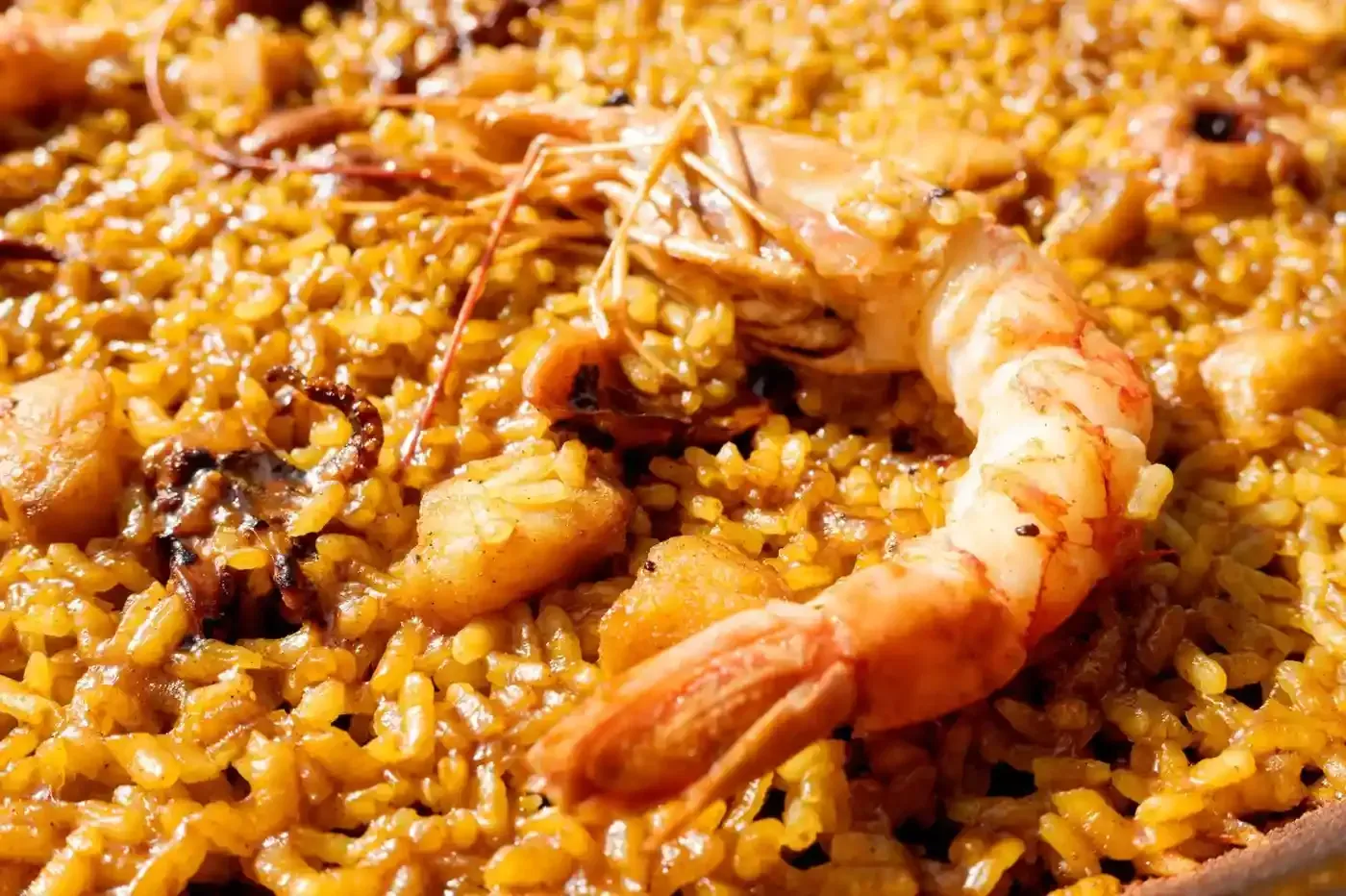 Paella con camarones, arroz y mariscos en una sartén de color marrón amarillento.