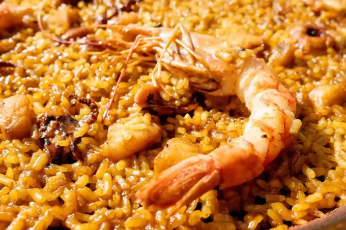 Paella con camarones, arroz y mariscos en una sartén de color marrón amarillento.