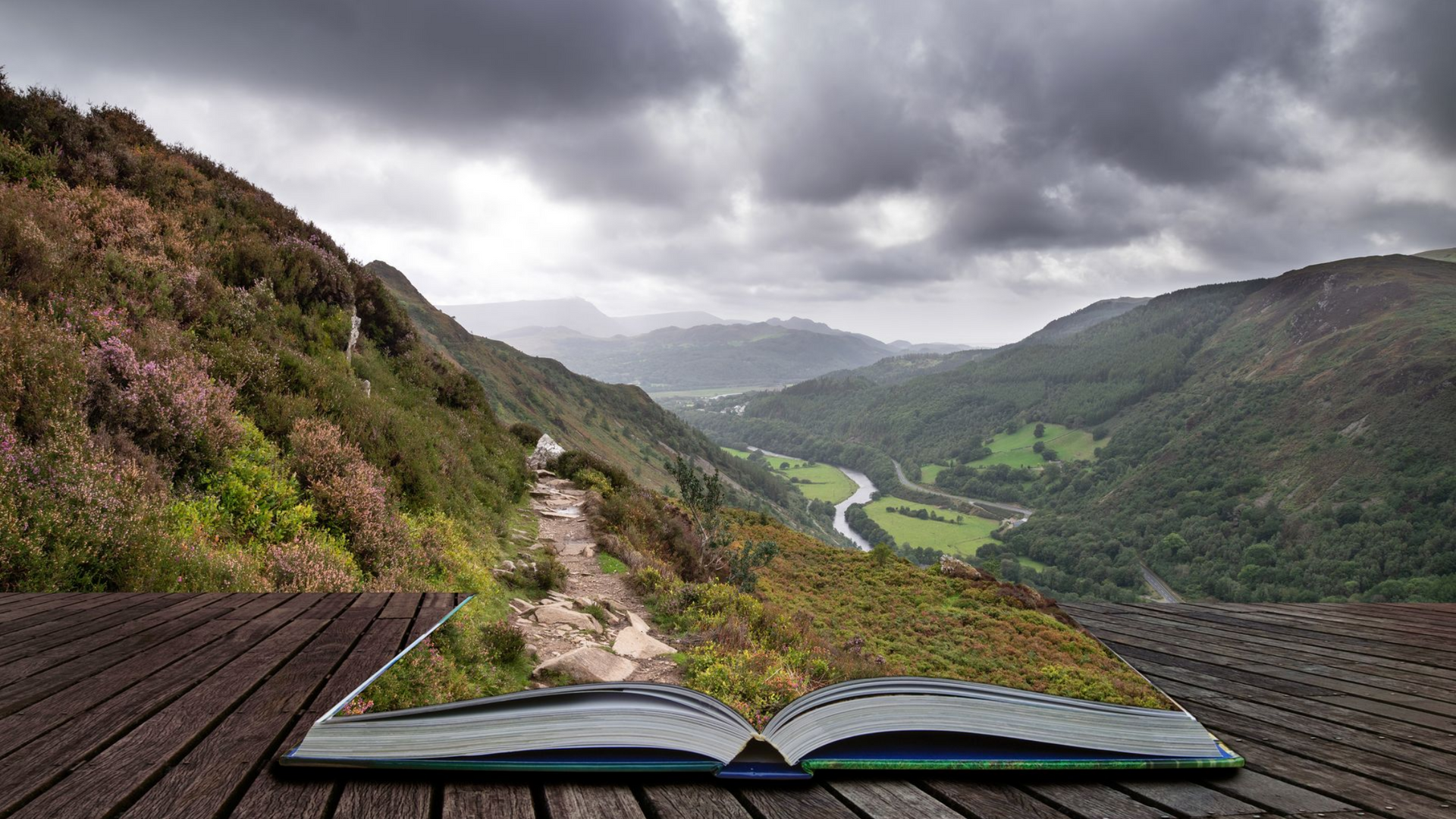Un livre ouvert offrant une vue imprenable sur les montagnes, un chemin sinueux et un ciel nuageux.