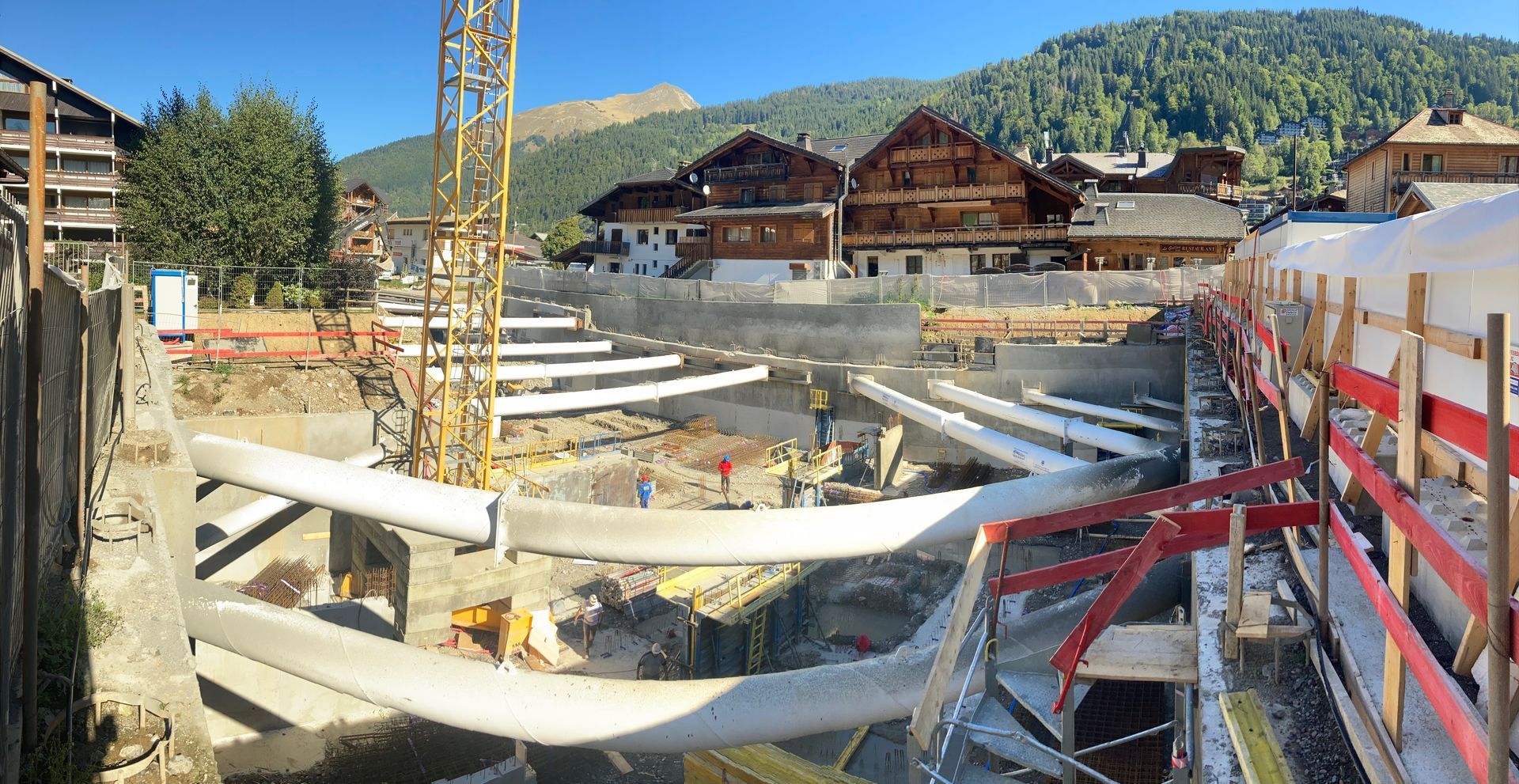 Pente recouverte d'une bâche anti-érosion, pylône de téléski partiellement construit et forêt environnante.