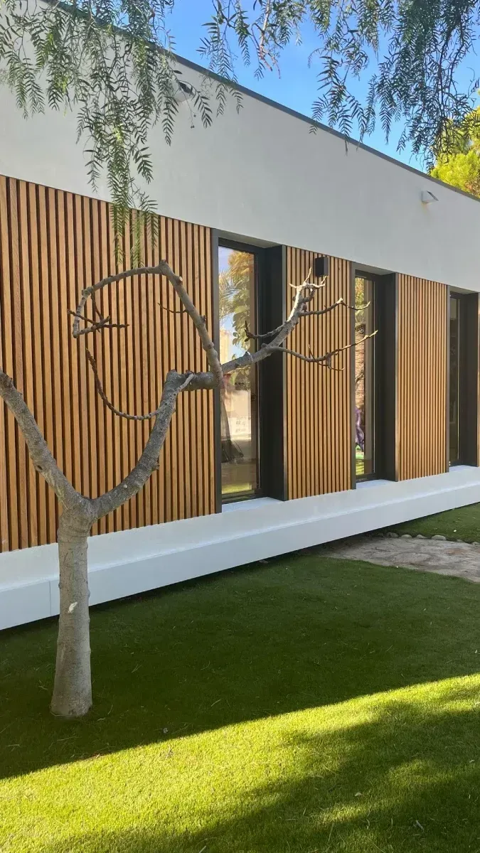 Un árbol frente a un edificio con revestimiento de madera.