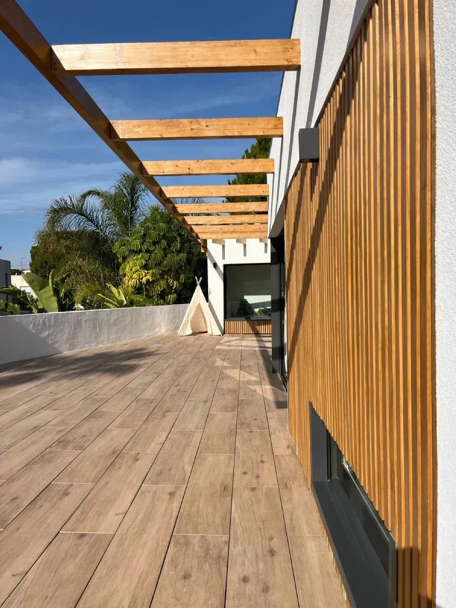 Una terraza de madera con una pérgola encima