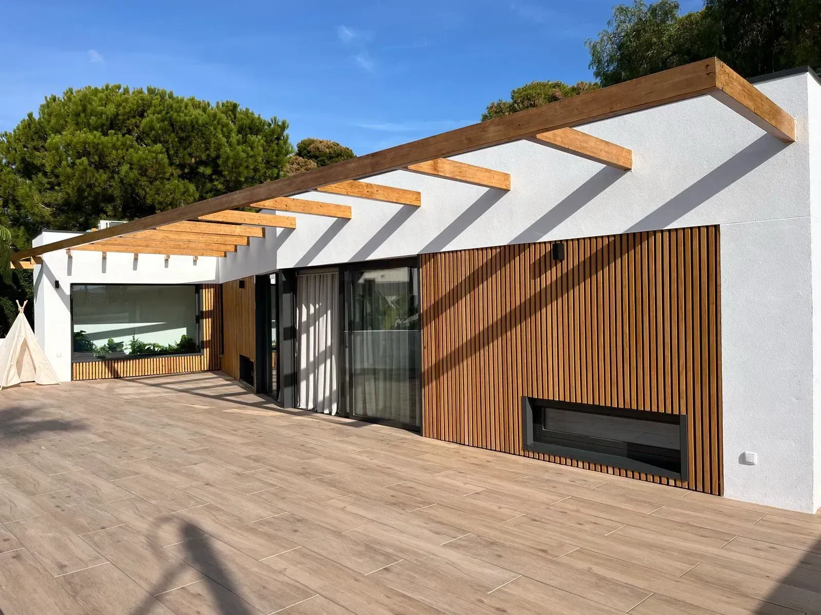 Una casa blanca con una pérgola de madera encima.