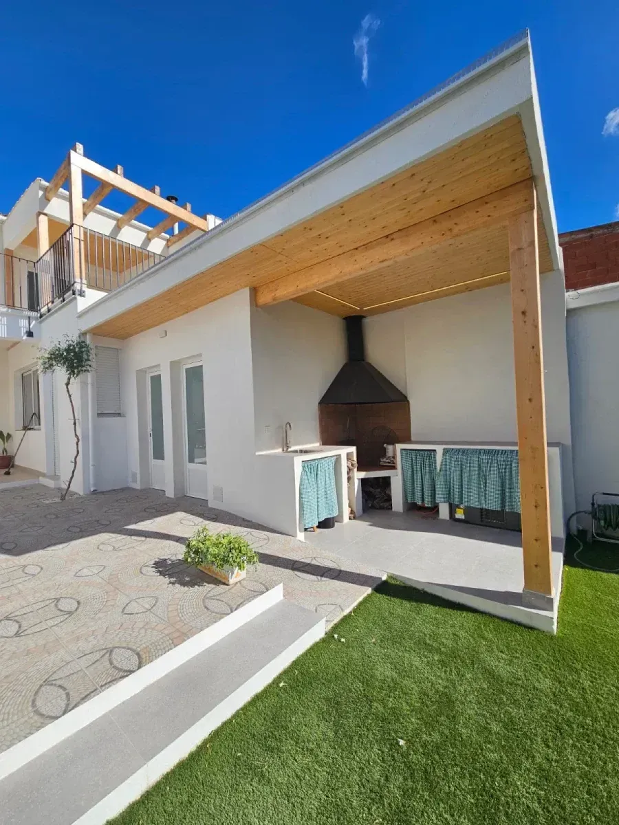Una casa blanca con una pérgola de madera y una barbacoa.