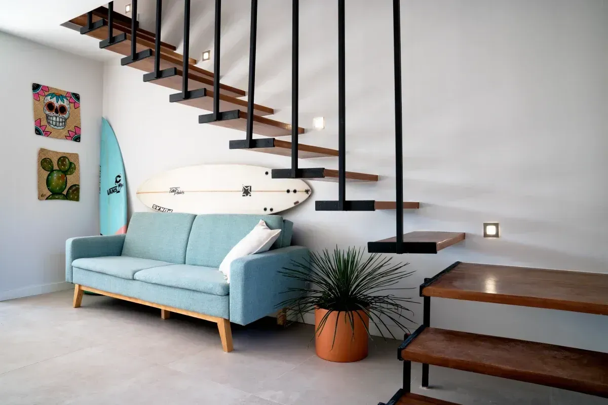 Una sala de estar con un sofá y escaleras y una tabla de surf en la pared.