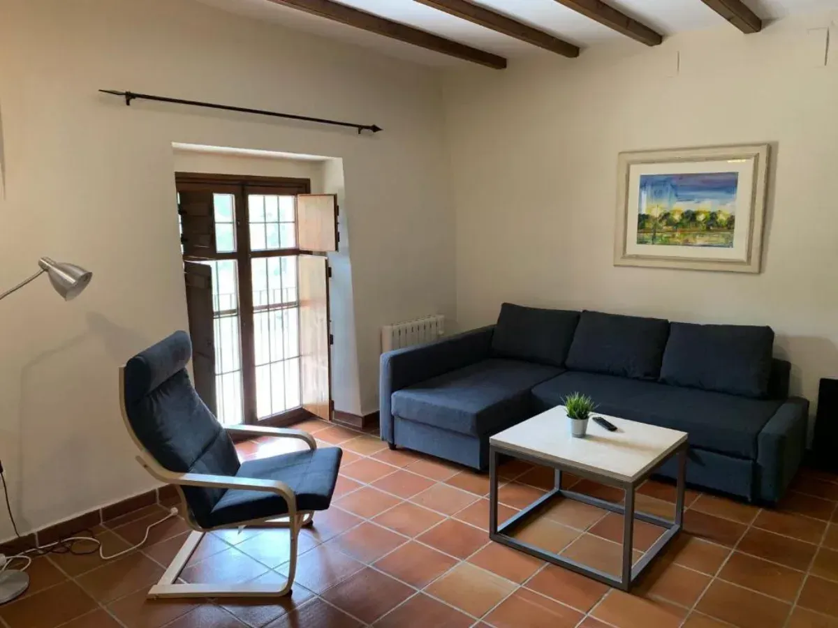 Sala de estar luminosa con sofá azul, sillón, mesa de centro, ventana, lámpara de pie y cuadros enmarcados en la pared.