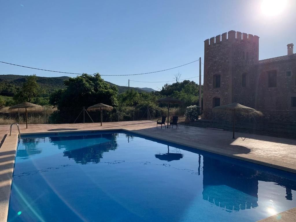 Piscina exterior soleada junto a un edificio de piedra y una ladera.