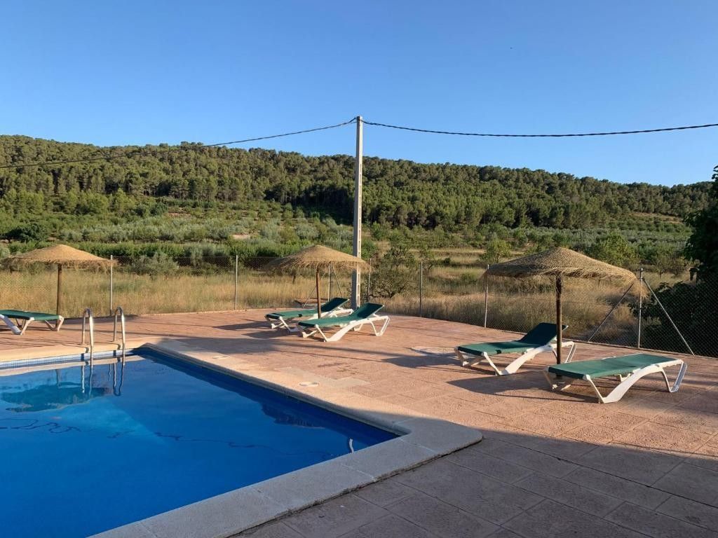 Piscina al aire libre con tumbonas y una colina al fondo bajo un cielo despejado.