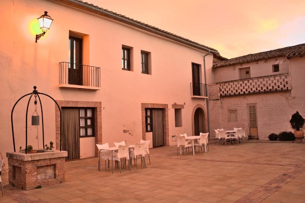 Patio al atardecer de una posada rústica de piedra con mesas y sillas al aire libre bajo un cálido cielo rosado.