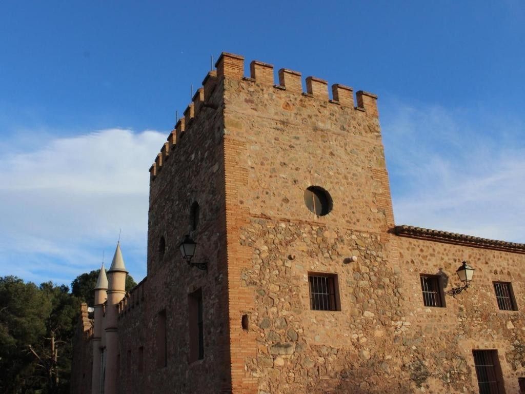 Torre de castillo de piedra con almenas bajo un cielo azul, con una ventana redonda y muros de ladrillo.