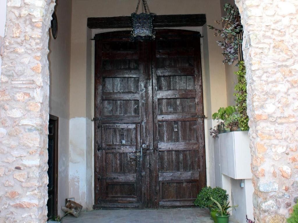 Puertas dobles rústicas de madera oscura enmarcadas por muros de piedra y plantas en macetas.