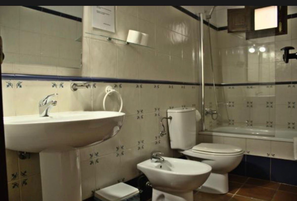 Baño pequeño alicatado con lavabo, inodoro, bidé, bañera y armario con espejo de pared.