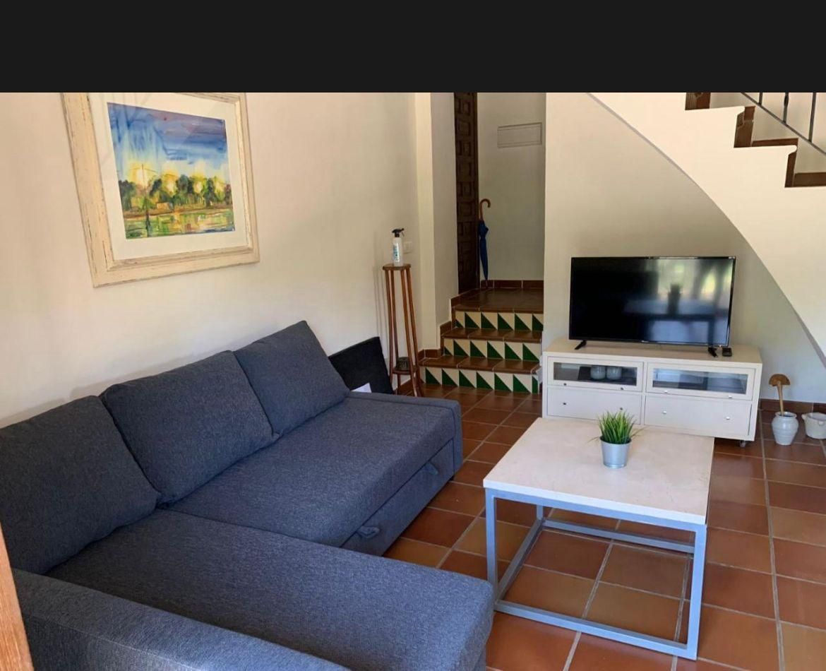 Sala de estar con sofá seccional gris, mesa de centro blanca, mueble para TV, suelo de baldosas de terracota
