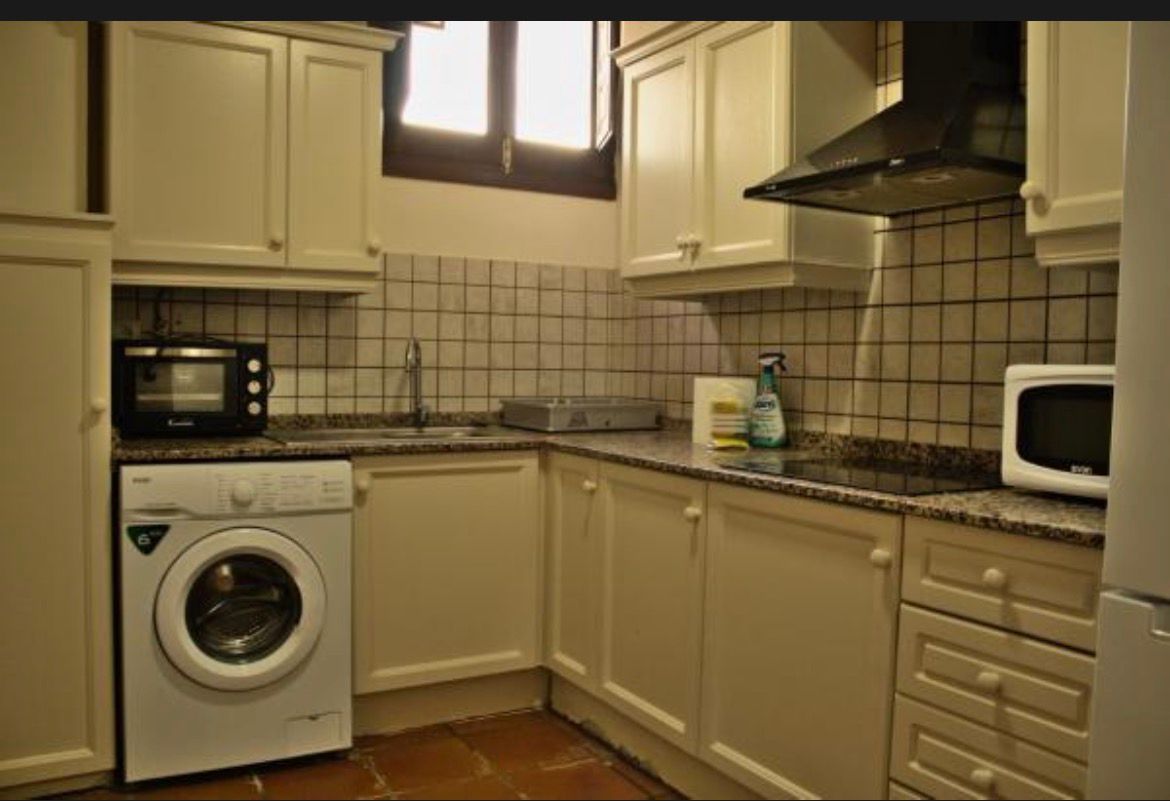 Cocina pequeña con armarios color crema, salpicadero de azulejos, lavadora, microondas