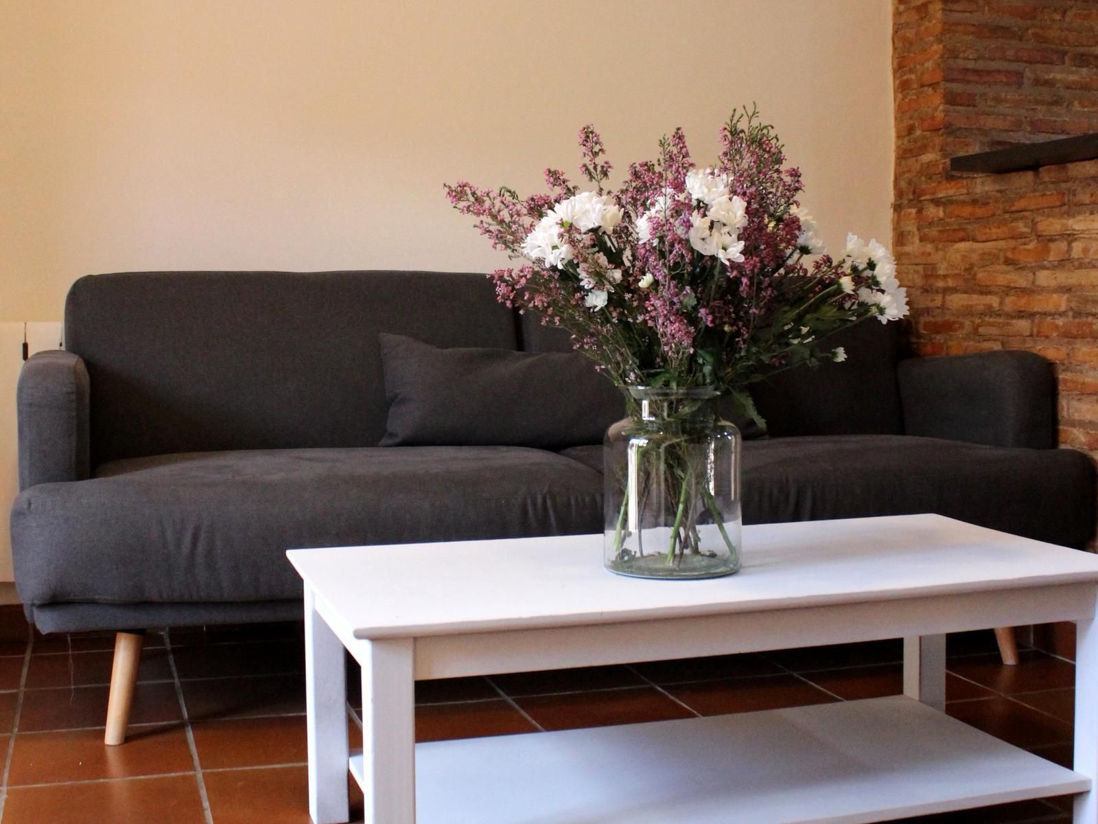Sala de estar con sofá gris oscuro, mesa de centro blanca y jarrón con flores rosas y blancas.