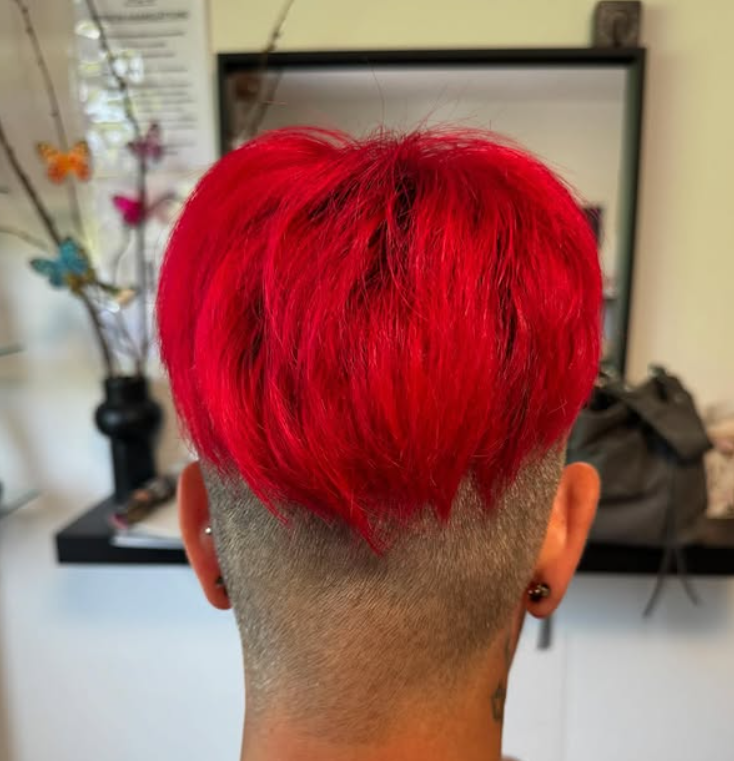 Person mit leuchtend rotem Haar und rasiertem Nacken in einem Salon.