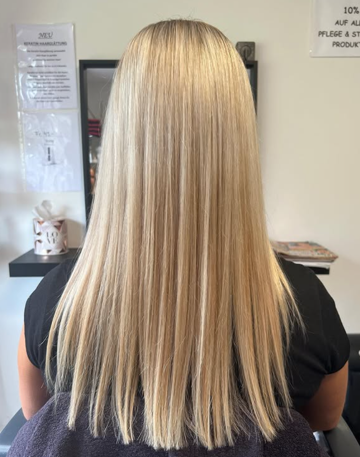 Frau mit langem, glattem, blondem Haar sitzt in einem Friseurstuhl.