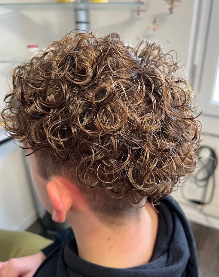 Ein Friseur schneidet mit einer Haarschneidemaschine die Haare eines Mannes am Haaransatz.