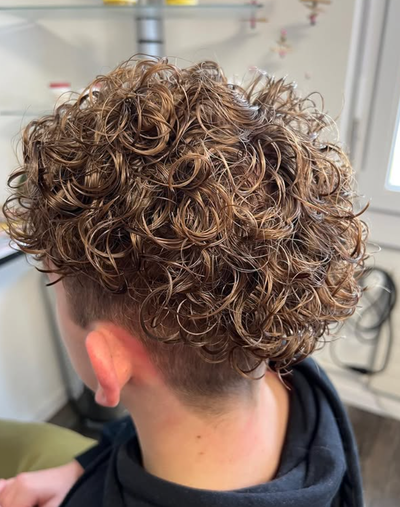 Ein Friseur schneidet mit einer Haarschneidemaschine die Haare eines Mannes am Haaransatz.