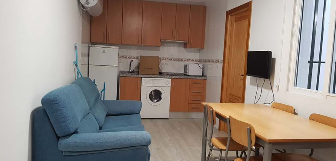 Una sala de estar con sofá, mesa, sillas y una cocina.