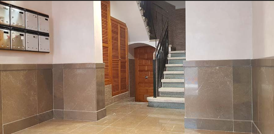 Un pasillo con escalera y buzones en la pared.