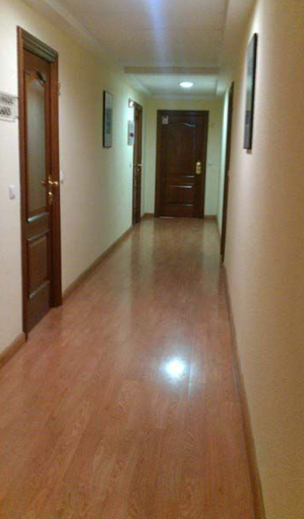 Un largo pasillo con suelos y puertas de madera.