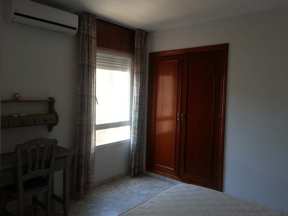 Un dormitorio con un escritorio y sillas y una ventana.