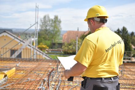 Mann in gelbem Shirt schaut auf Pläne, trägt, Elektro Knuchel AG